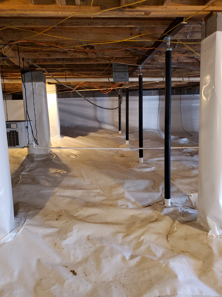 Crawl space with vapor barrier and support beams, wooden ceiling, and visible wiring.