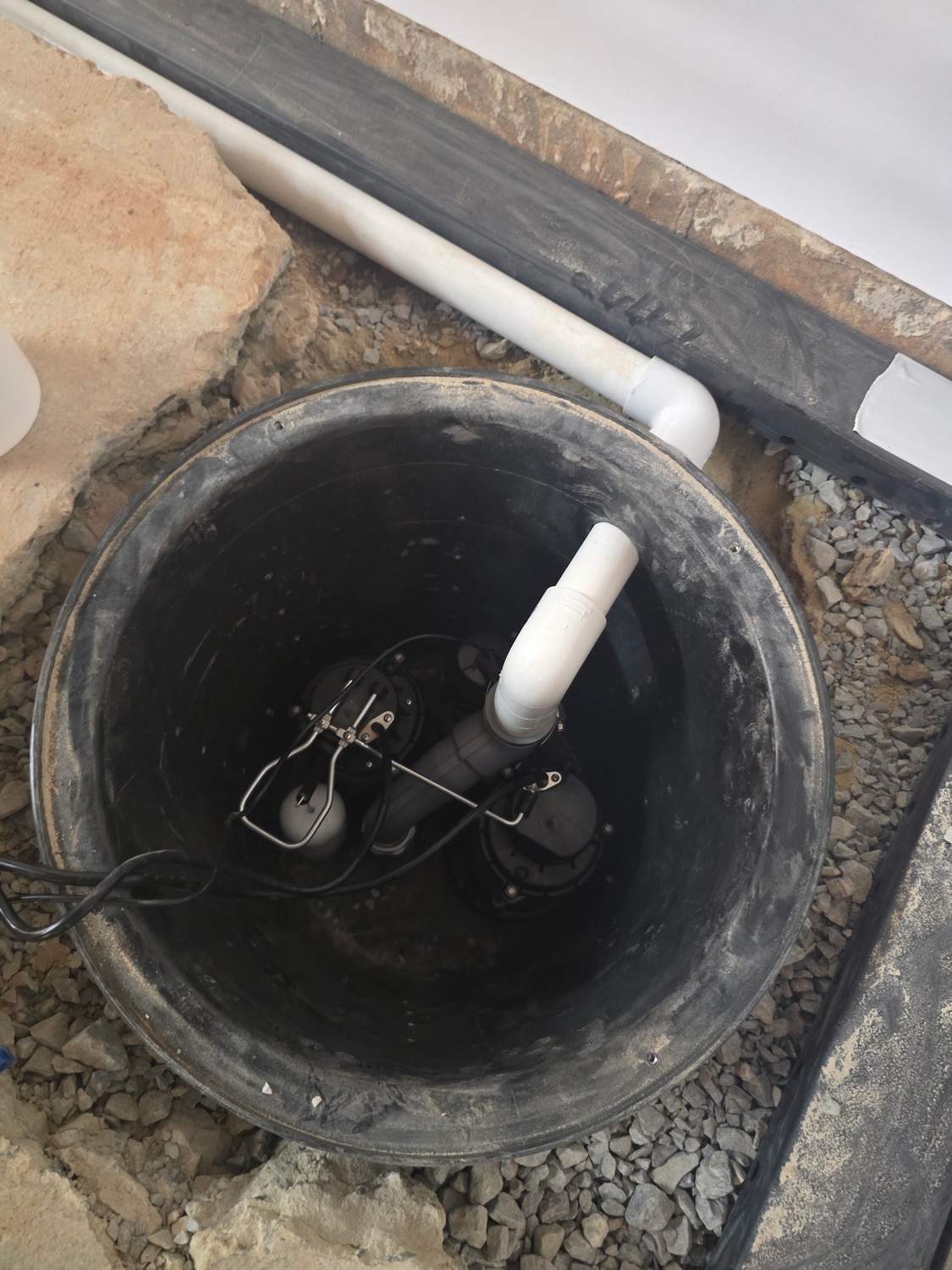 Sump pump installation with PVC piping in a basement drainage pit.