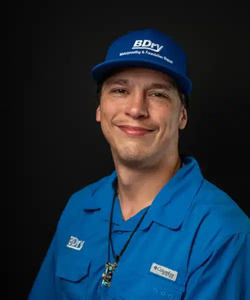 Man in blue uniform and cap with logo, black background, smiling.