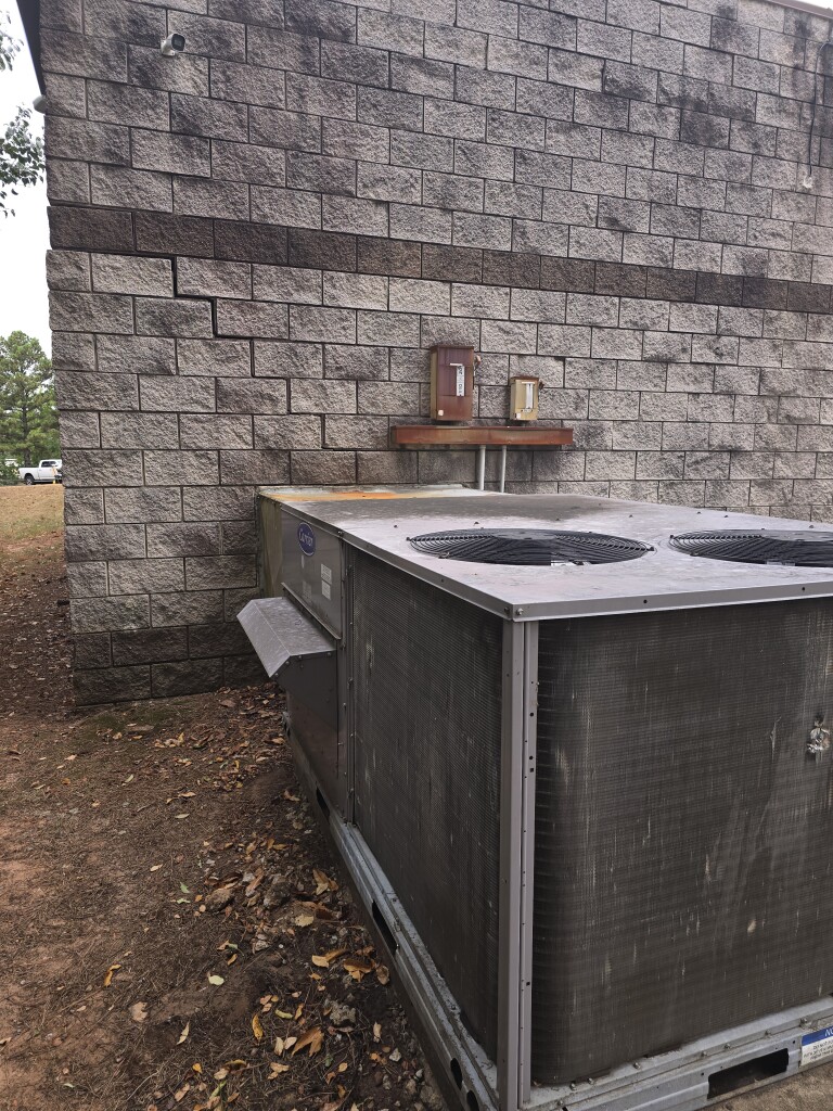 Outdoor HVAC unit next to a brick building with autumn leaves on the ground.