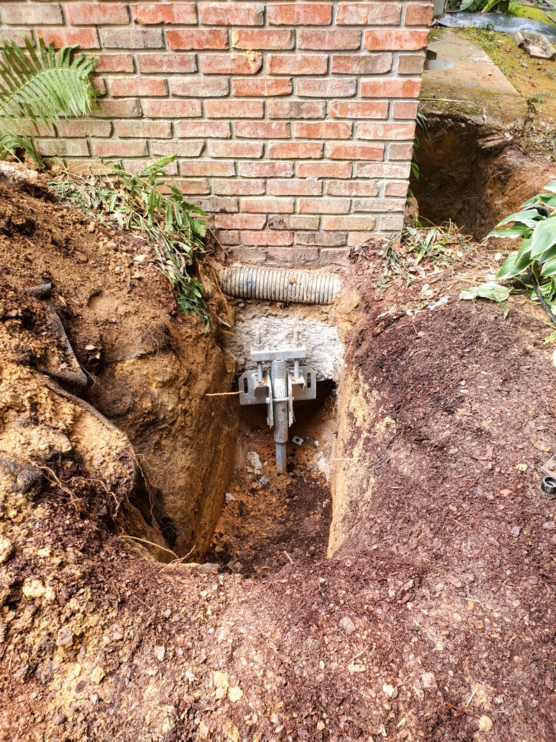 Foundation repair with helical pier installation near brick wall for stabilization.
