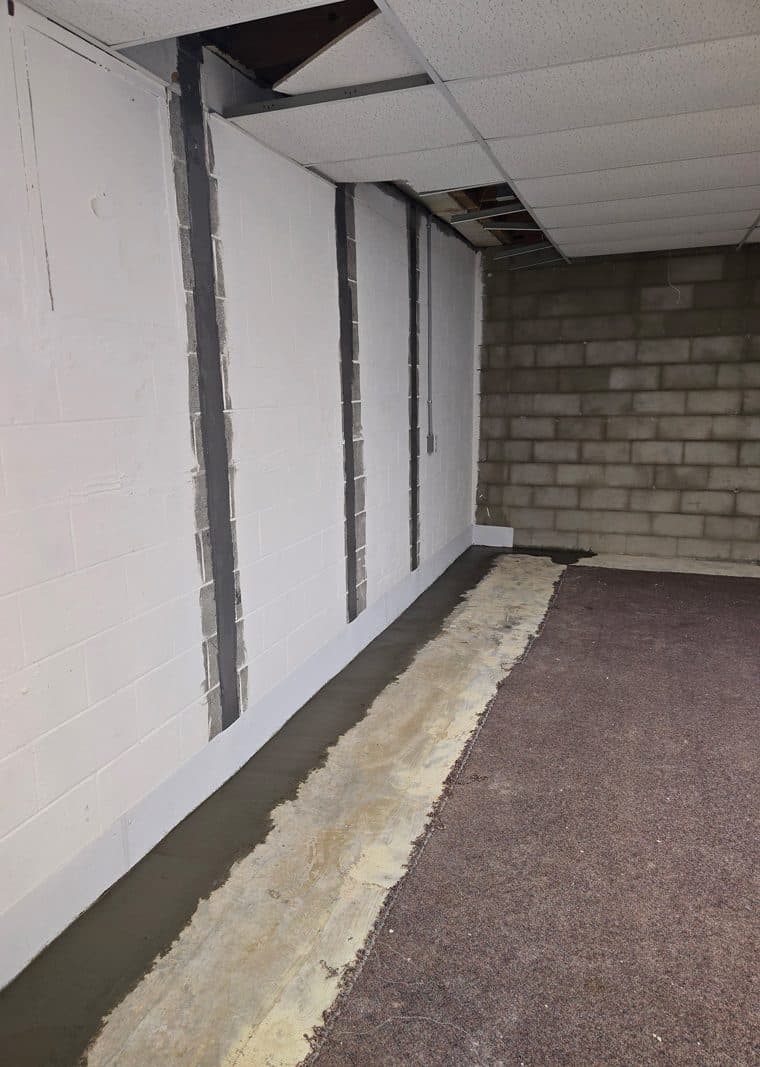 Basement under renovation with exposed ceiling panels and a new concrete strip along the wall.