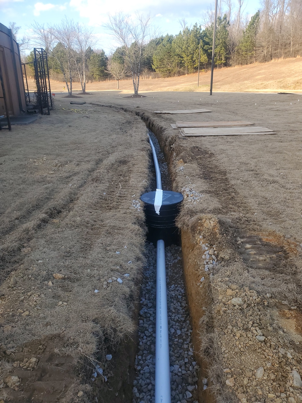 Underground drain pipe installation in progress on grassy landscape with trees in background.
