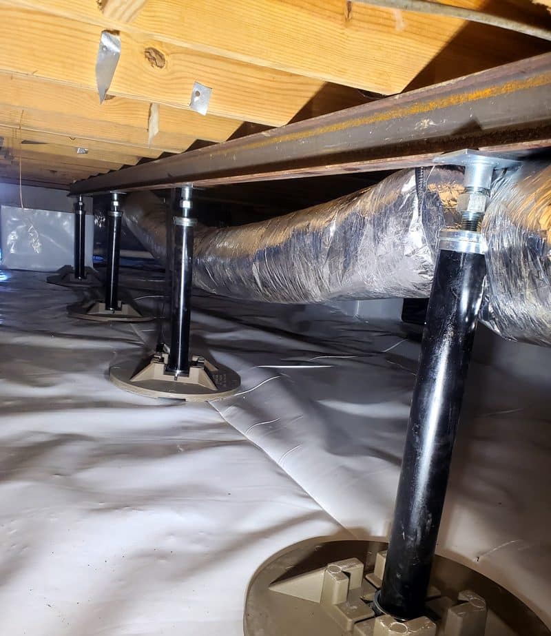 Crawl space with support jacks and insulated ductwork under a wooden beam.