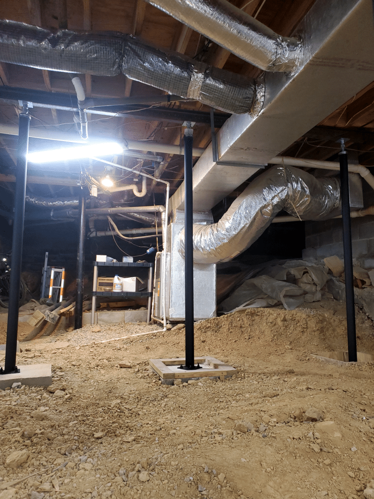 Basement view with exposed ductwork, structural supports, and dirt floor, indicating ongoing construction.