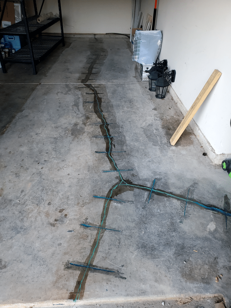 Cracked concrete garage floor with visible repairs and storage items along the wall.