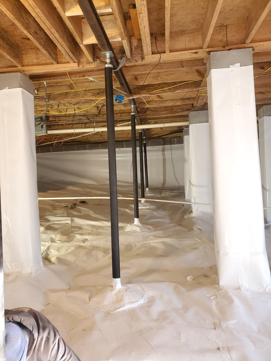 Crawl space with plastic encapsulation, support beams, and exposed wooden joists.