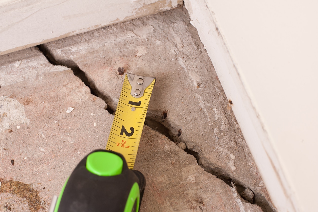Measuring tape placed on cracked concrete floor near wall.