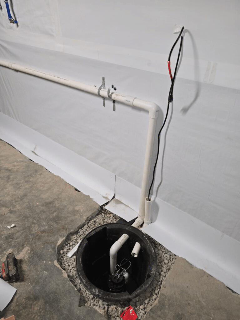 Basement sump pump installation with PVC pipes and wiring setup against a sealed wall.