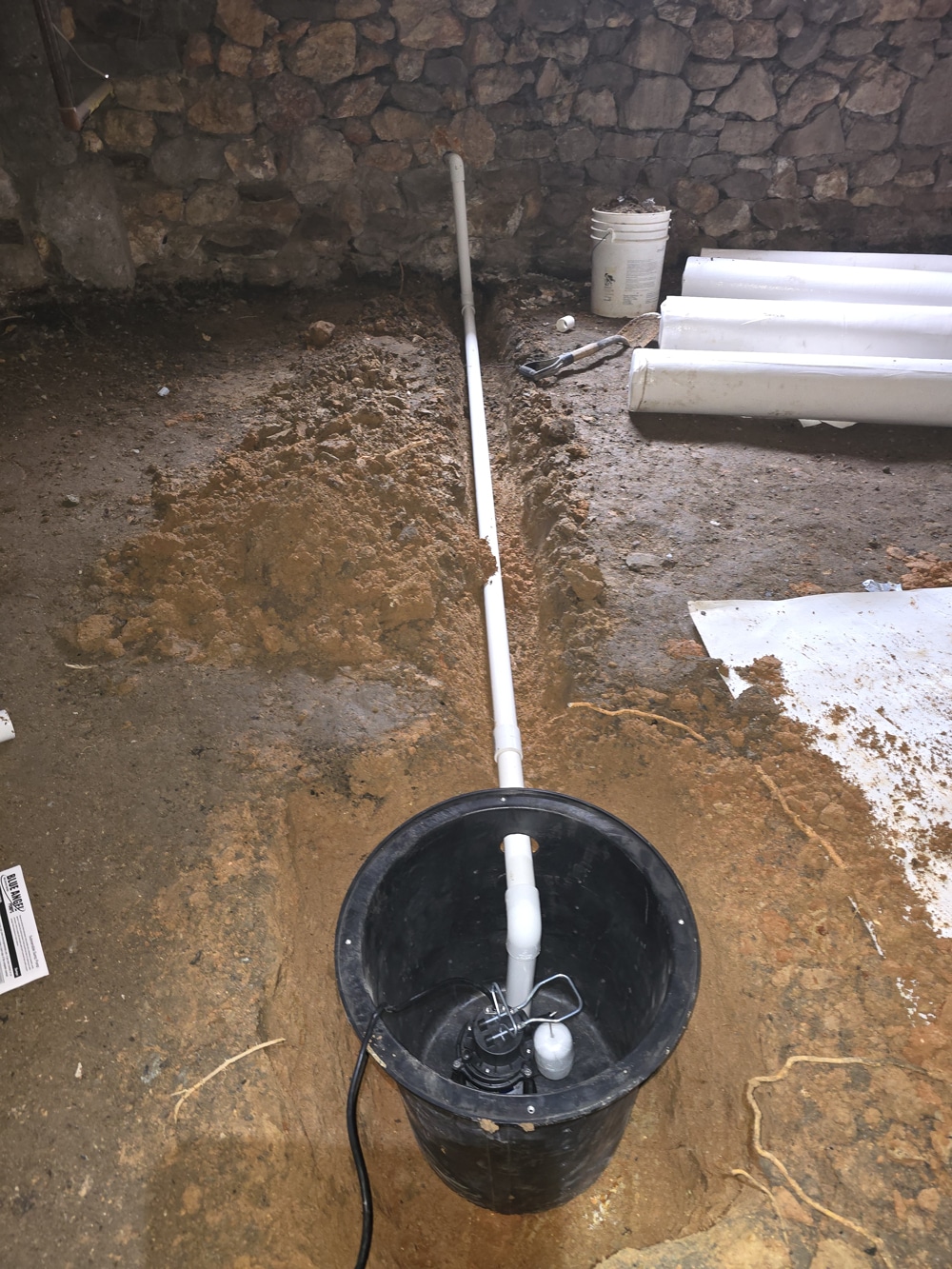 Sump pump installation in a basement with PVC pipe and tools on concrete floor.
