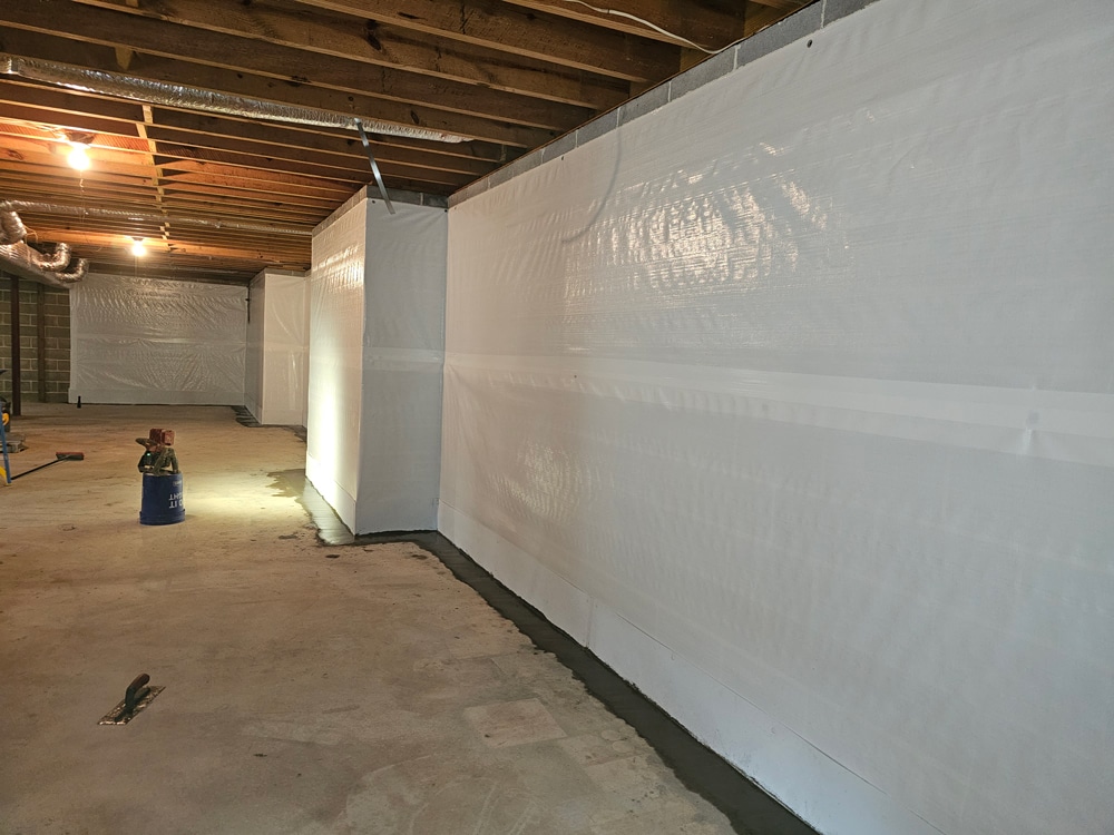 Basement waterproofing project with white liner and exposed wooden ceiling beams.