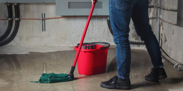 A woman mopping a flooded basement with water leaking through cracked concrete walls — a serious basement moisture problem.